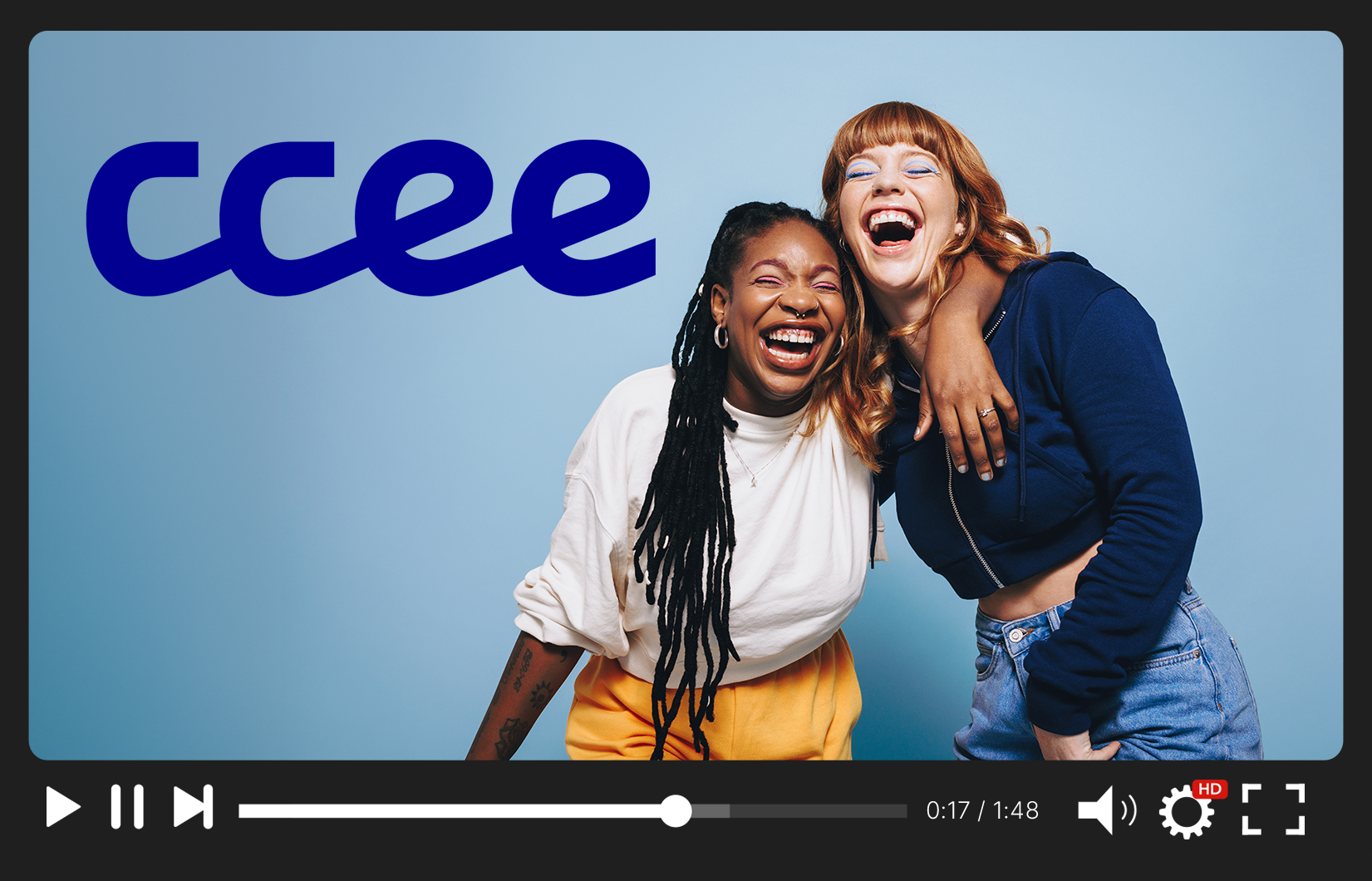 A foto mostra duas mulheres, uma negra e uma branca, se abraçando ao lado do logo da CCEE