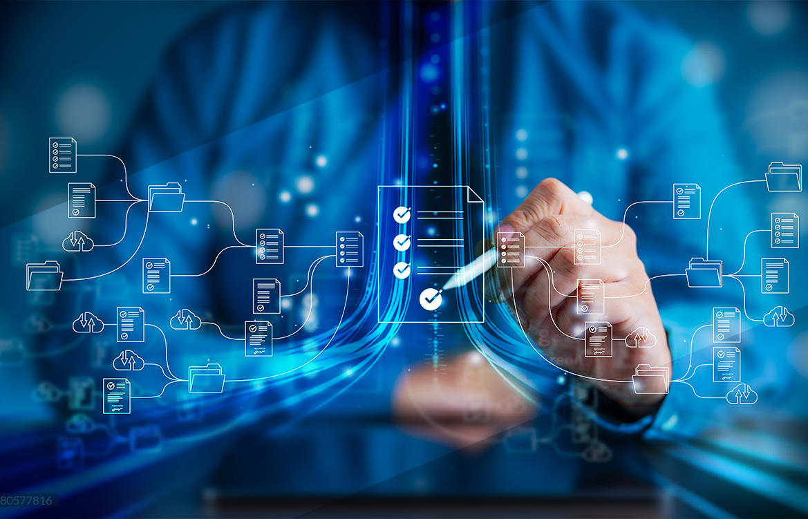 A imagem mostra o torso de um homem que veste uma camisa azul. Ele está sentado e tem, em suas mãos, uma caneta usada em tablets. Na sua frente, há uma montagem holográfica que remete a gráficos e tabelas.